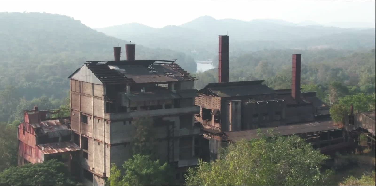 Drone view of the crumbling old factory ruin framed by dense forest