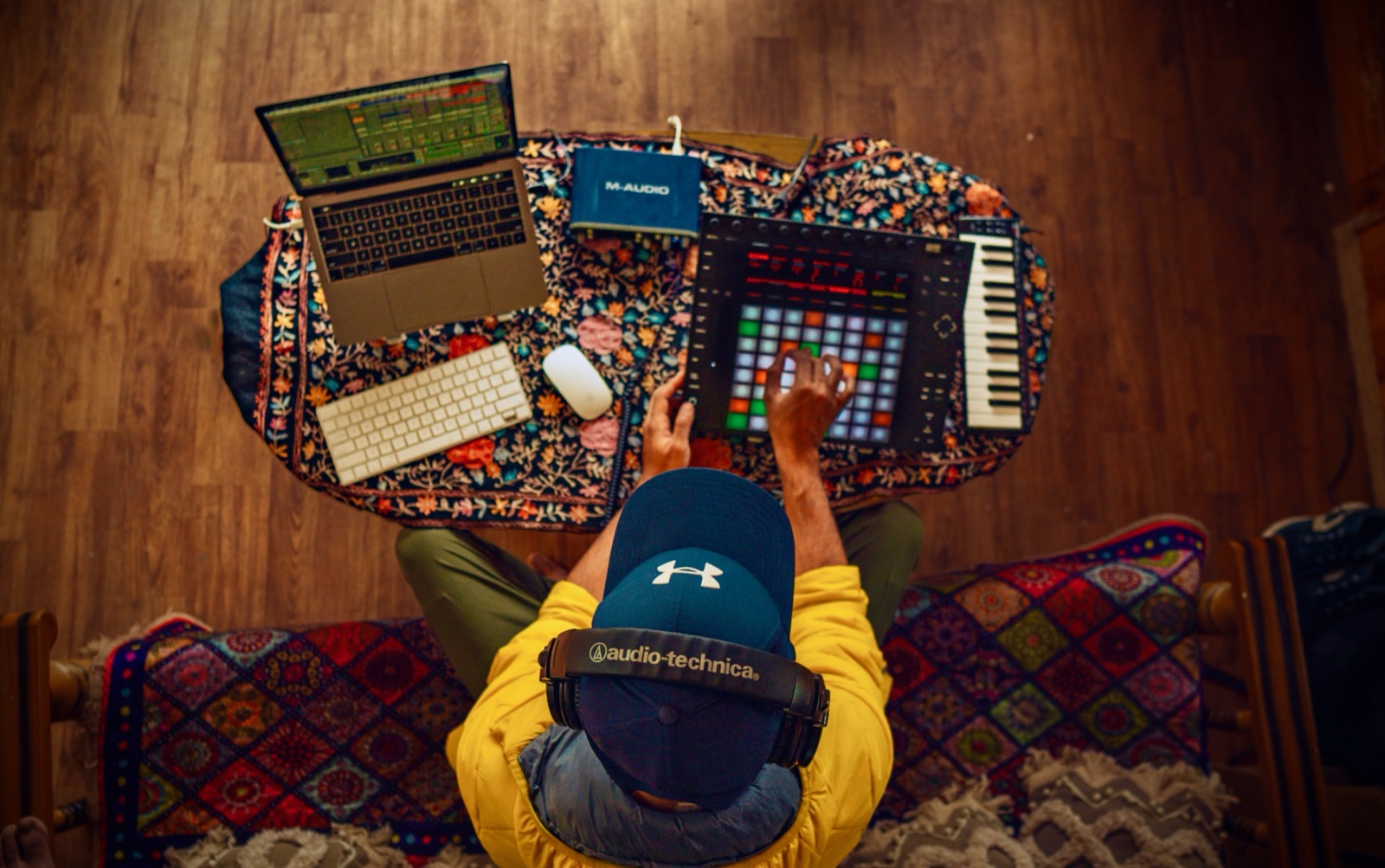 A whole rig laid out on the rug: laptop, pads, keys, headphones