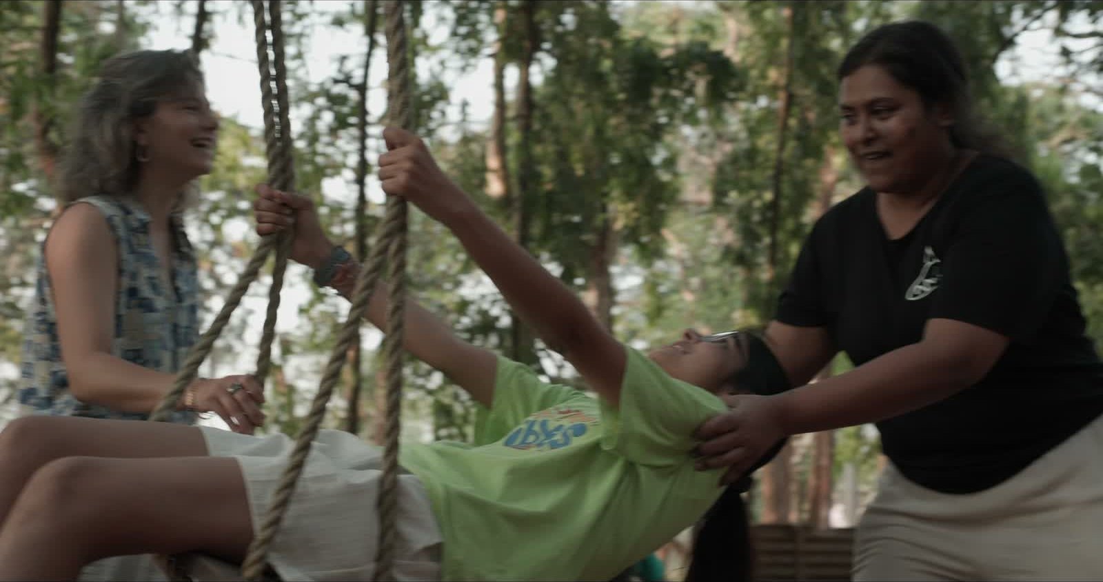 Two women and a child laughing on a rope swing in the forest at Jungli
